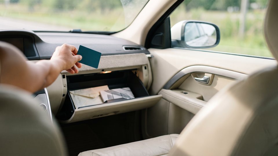 A hand places a blank card into an open glove box inside a car