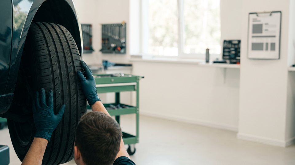 Gloved hands check a tire on a car in a clean repair garage, seen from behind